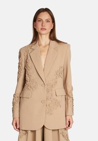 Blazer bej cu broderie florală pe umeri și mâneci, două buzunare frontale și două nasturi; croială ajustată cu un design structurat.