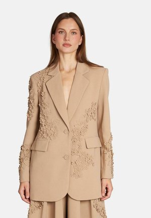 Blazer beige con bordados florales en los hombros y las mangas, dos bolsillos frontales y dos botones; corte entallado con un diseño estructurado.