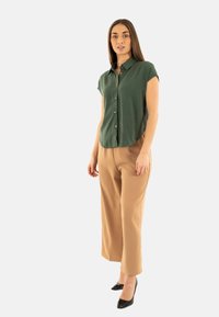 Camicia verde a maniche corte con bottoni realizzata in tessuto testurizzato, abbinata a pantaloni beige a gamba larga e scarpe con tacco a punta nere.