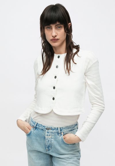 Λευκό κοντό μπουφάν με κούμπωμα με κουμπιά μπροστά, μακριά μανίκια και στρογγυλεμένη ρίγα, συνδυασμένο με ανοιχτό μπλε ψηλόμεσα τζιν παντελόνια. Απλός σχεδιασμός.