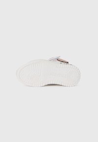 Semelle de basket blanche en caoutchouc texturé, avec des motifs circulaires et des accents surélevés. Une sangle Velcro est visible au-dessus de la semelle.