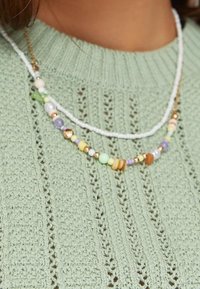 Multi-layered beaded necklace featuring pastel-colored beads, gold accents, and two distinct chains, worn over a light green knitted sweater.