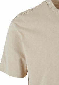 Tricou bej cu mânecă scurtă, fabricat dintr-un material neted din bumbac mixt. Dispune de un gât clasic de tip crew și cusături îngrijite pe margine și la mâneci.