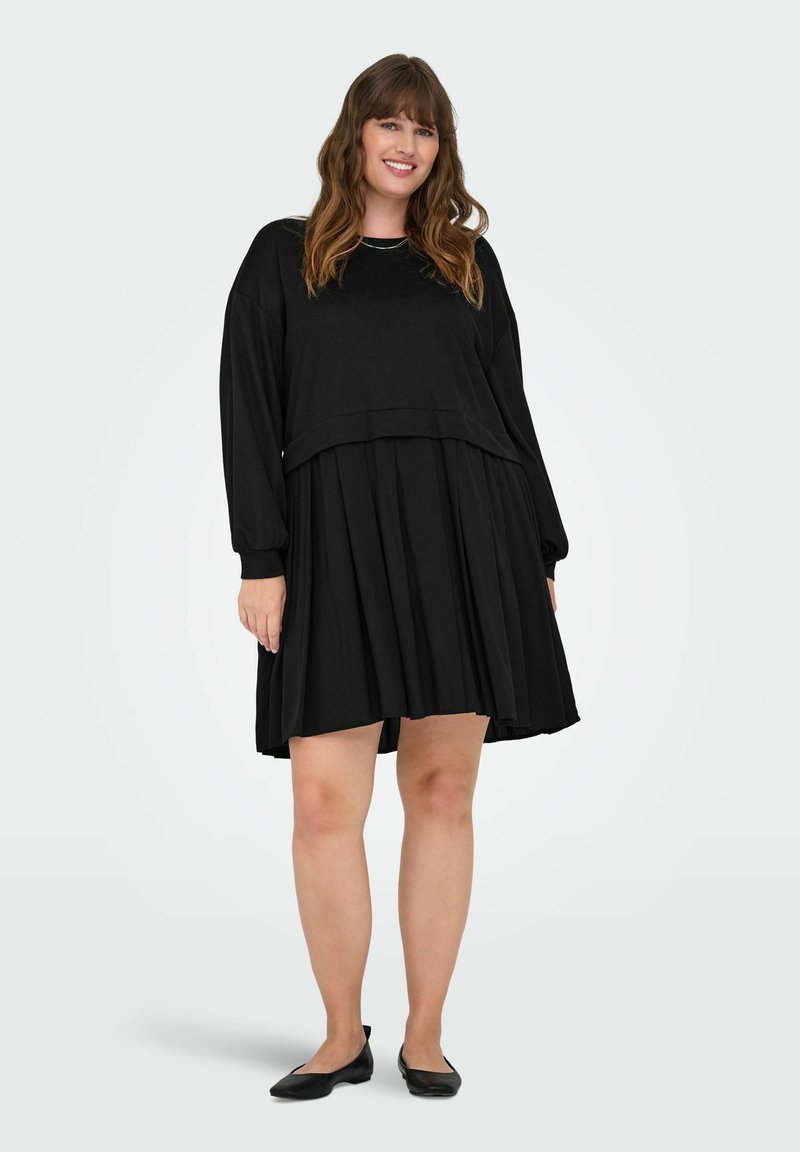 Abito nero con top corto a maniche lunghe e gonna plissettata. Realizzato in materiale morbido, ha una texture liscia e una vestibilità comoda.
