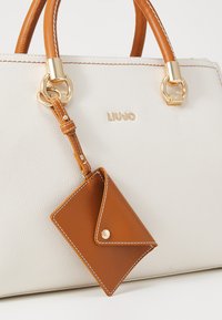 Borsa a tracolla in pelle bianca testurizzata con manici in pelle marrone, dotata di hardware dorato e un portacarte brown staccabile con cuciture bianche.