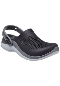 Czarne perforowane klapki z szarą podeszwą, z tylnym paskiem i gładką fakturą dla komfortu. Etykieta z boku głosi "Crocs."