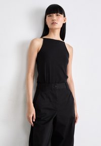 Svart, tettsittende tanktopp med tynne stropper og firkantet utringning, paret med høytlivede, svarte vide bukser. Glatt, stretchy stoff.
