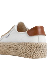 Hvitt lerret sneakers med en flettet jutefot og en brun lærdetalj på hælen. Har runde snørebånd og minimal merkevare.