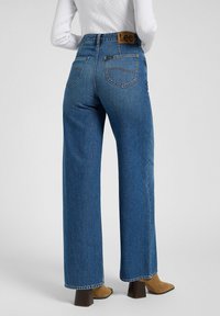 Jeans blu a vita alta e gamba larga in denim, con un'etichetta in pelle marrone del marchio Lee e tasche posteriori visibili.