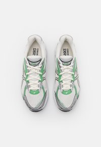 Zapatillas de correr con parte superior de malla en blanco con acentos en verde y gris, y una suela acolchada para mayor comodidad. Diseño con cordones y detalle del logo.