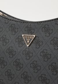 Black textured handbag featuring a prominent gold triangular "GUESS USA" logo on the front, with a zippered top and subtle pattern.