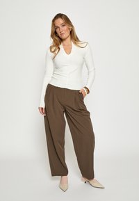 Hvid langærmet top med V-hals og ribbet tekstur, kombineret med brune bukser med brede ben. Modellen har beige sko med spids tå på.