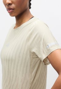 Μπεζ αθλητικό πουκάμισο με υφασμένη διαγώνια υφή, κοντά μανίκια και αντανακλαστικές λεπτομέρειες στους ώμους. Απαλό ύφασμα με εφαρμοστή σχεδίαση.