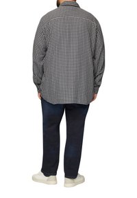 Langarm geruite shirt in zwart en wit met een ontspannen pasvorm, gecombineerd met donkere jeans en witte sneakers.