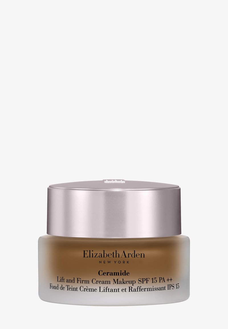 Kleines mattiertes Glas mit Elizabeth Arden Ceramide Lift and Firm Cream Makeup mit LSF 15 und glänzendem silbernem Deckel auf weißem Hintergrund.