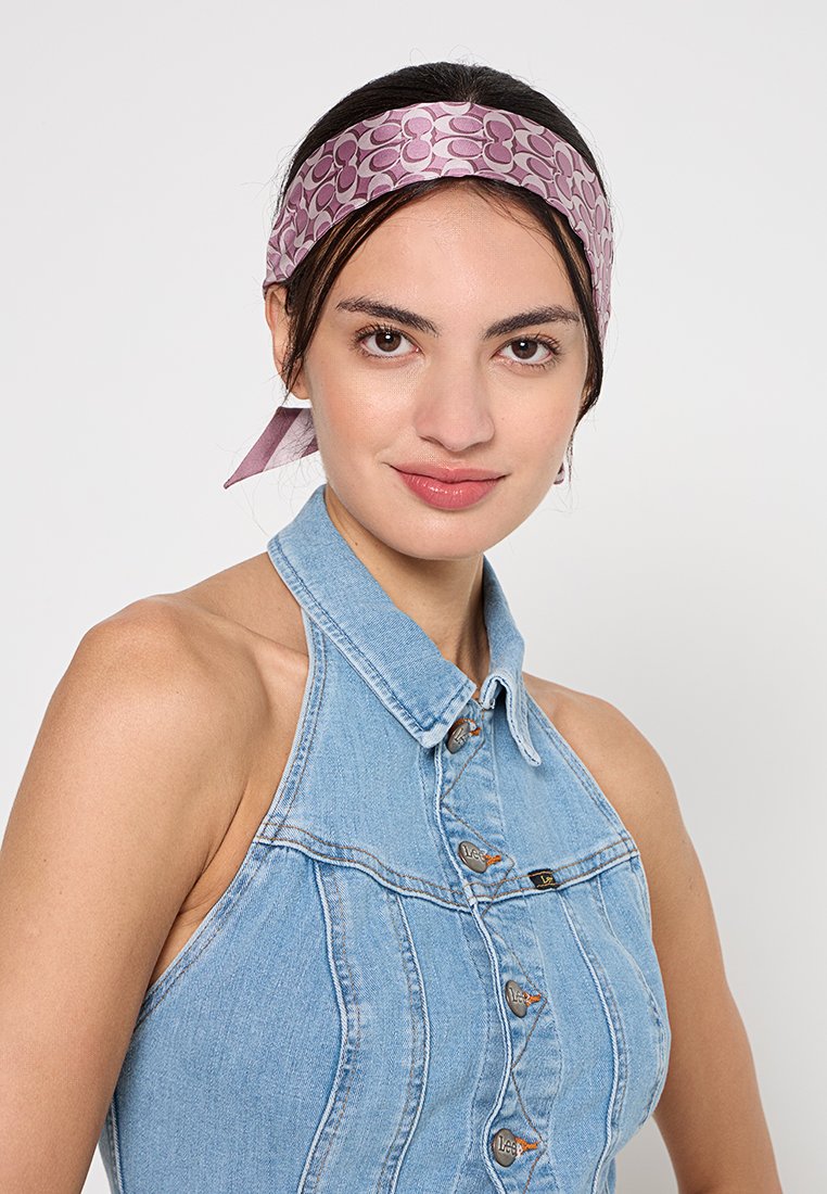 Rosa gemusterter Seidenschal, der um den Kopf gebunden ist, mit kreisförmigen Designs. Wird mit einem Denim-Haltertop getragen. Glatte Textur, glänzende Oberfläche.