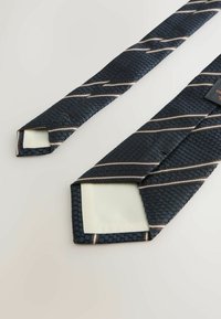 Mørkeblå slips med en tekstureret overflade, forsynet med skrå lysebrune striber. Enderne er spidse med en glat stof underside.