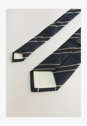 Námořnická modrá kravata s texturovaným povrchem, na kterém jsou diagonální světle hnědé pruhy. Konce jsou špičaté a z druhé strany je hladký materiál.