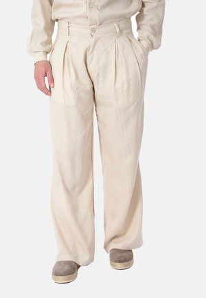 Pantaloni beige a gamba larga plissettati con bottone e cerniera sul davanti, indossati con una camicetta abbinata e scarpe espadrillas taupe.