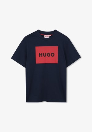 Teget pamučna majica s pravokutnim crvenim logotipom na kojem se u središtu nalazi tekst "HUGO" ispisan podebljanim crnim slovima. Kratki rukavi i okrugli izrez.