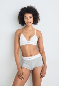 Bela rebrasta trianglasta bralette z tankimi naramnicami in sivo visoko pasovi kratkimi hlačami, ki imajo bel logotip. Enostaven, oprijet dizajn.