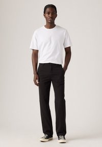Witte katoenen t-shirt, zwarte rechte broek en zwarte sneakers. Eenvoudig ontwerp, effen kleuren en geen zichtbare patronen of accenten.