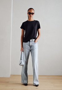 Zwarte korte mouwen t-shirt, lichtblauwe wijde jeans, zwarte pumps met spitse neus, oversized zwarte zonnebril en een lichtgrijze handtas.