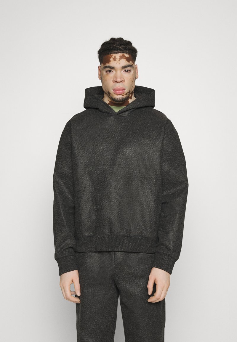 Sudadera gris texturizada con bolsillo canguro y capucha con cordón. Puños y dobladillo acanalados, combinada con pantalones a juego.