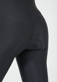 Zwarte sportleggings gemaakt van rekbare stof, met een gladde textuur, hoge tailleband en versterkte stiksels langs de naden.