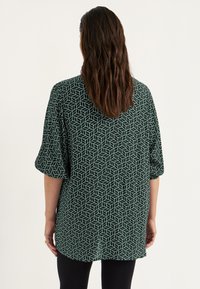 Groen, geometrisch patroon kortekorte mouw top met een losse pasvorm en zachte textuur, voorzien van een ronde halslijn en een ontspannen silhouet.