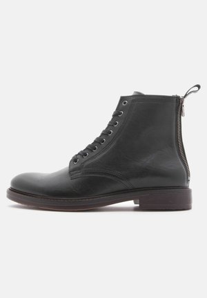 Botas de tobillo de cuero negro con punta redonda, cordones en la parte delantera y cremallera lateral. Textura suave con un ligero brillo y suela resistente.