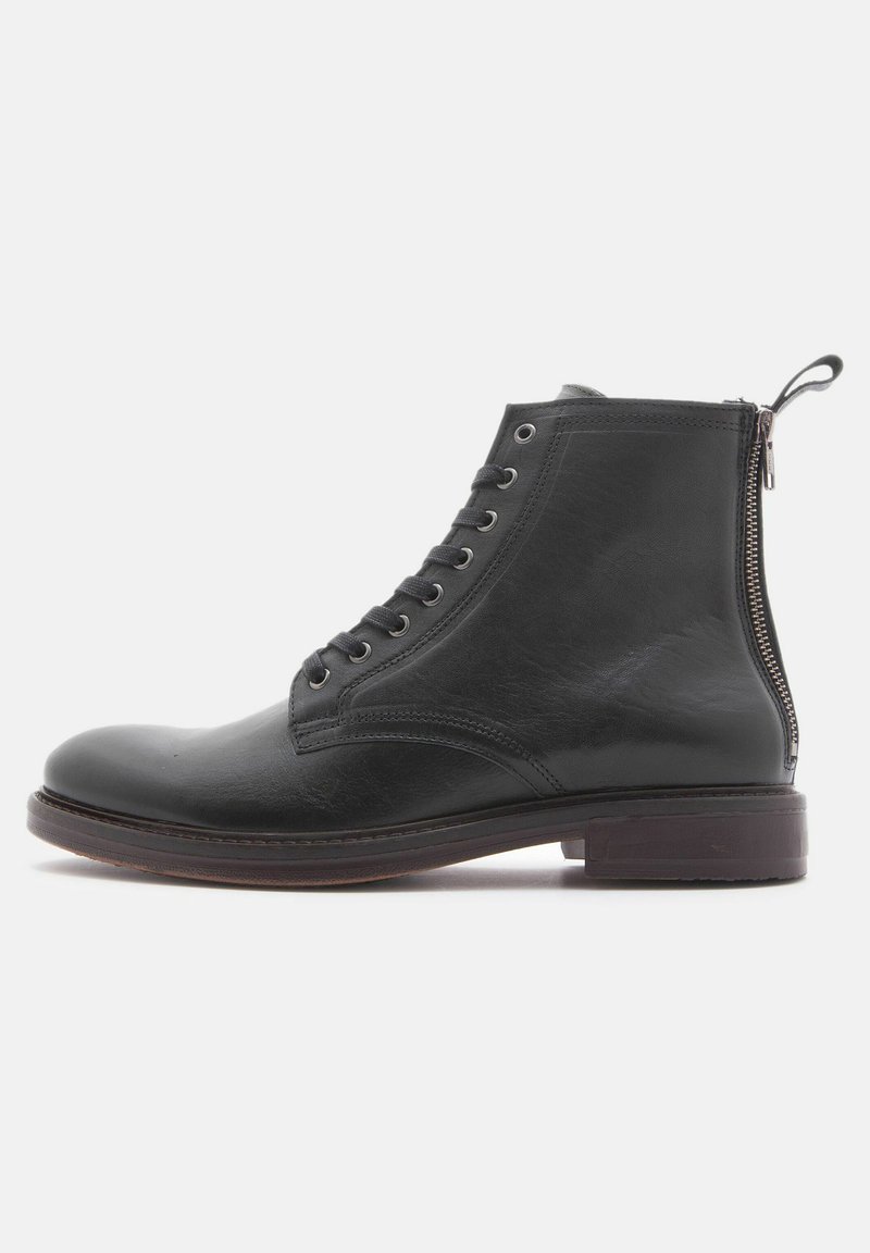Borchie in pelle nera alla caviglia con punta arrotondata, allacciatura frontale e zip laterale. Texture liscia con una leggera lucentezza e suola robusta.