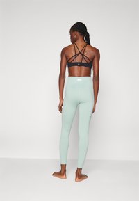 Top sportivo nero con schienale incrociato, abbinato a leggings a vita alta di colore verde menta, a costine. Design semplice, senza motivi visibili o hardware.