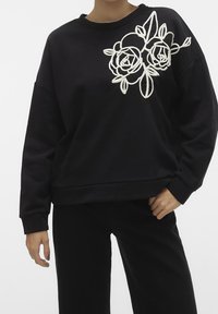 Sudadera negra de manga larga, con rosas bordadas en blanco en el lado izquierdo. Corte holgado, cuello y puños acanalados.
