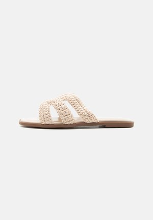 Beige flad slidssandal med en tekstureret vævet overdel og glat sål, vist på en ensartet, lys baggrund.
