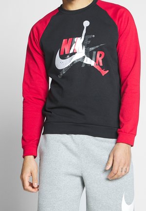 Sudadera negra con mangas raglán rojas. Presenta un gran logo de Nike Air en blanco y rojo en el pecho. Material de algodón suave.
