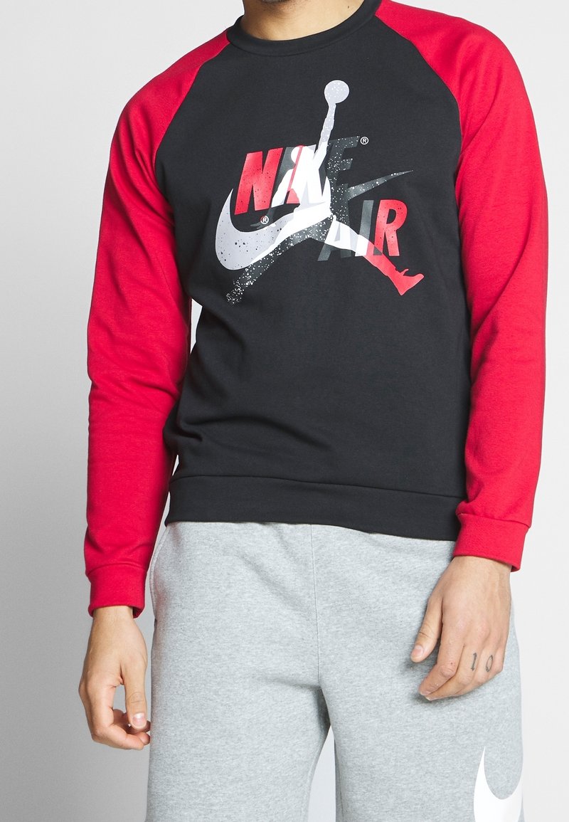 Sudadera negra con mangas raglán rojas. Presenta un gran logo de Nike Air en blanco y rojo en el pecho. Material de algodón suave.