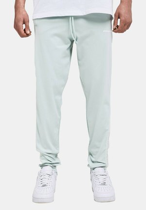 Mann trägt hellgraue, schmal zulaufende Jogginghosen mit Kordelzug und weiße Turnschuhe, steht mit entspannten Armen an den Seiten.