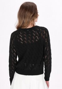 Maglione nero a maglia con un motivo in pizzo, maniche lunghe e design corto. La texture è a maglia aperta con orlo a coste.