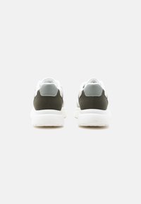 Ζευγάρι λευκά αθλητικά παπούτσια με γκρι και σκουροπράσινες λεπτομέρειες, από οπίσθια όψη σε απλό ανοιχτό γκρι φόντο.
