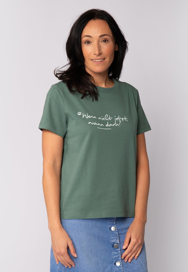 T-shirt en coton vert à manches courtes, col rond, avec un texte blanc dans une police décontractée. Assorti à une jupe en denim.