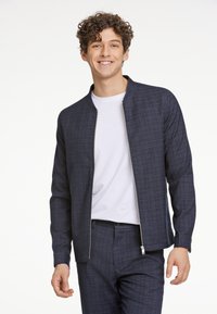 Marinblå bomberjacka med rutmönster, har dragkedja fram, ribbad krage och långa ärmar. Matchas med byxor i samma stil.