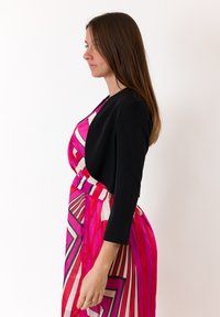 Blazer nero a maniche lunghe abbinato a un vestito rosa e bianco con motivo a zigzag e una cintura elastica.