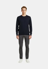 Maglione in maglia blu navy con collo rotondo, polsini e orlo a coste. Abbinato a pantaloni grigi e sneakers bianche per un look casual.