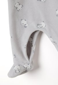 Mono de felpa gris con estampado de panda. Presenta broches de cierre en la parte inferior y diseño con pies. Textura suave, gris claro con acentos oscuros.
