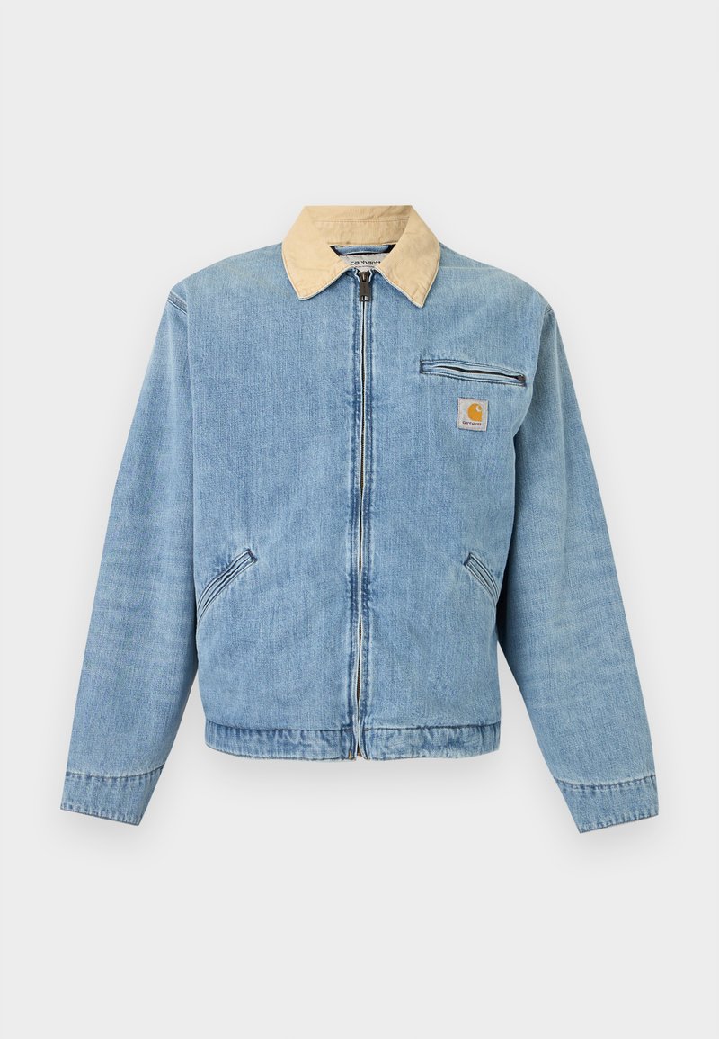Lichtblauwe spijkerjas met beige kraag, ritssluiting aan de voorkant, twee onderste zakken, horizontale ritssluitingzak en Carhartt-logo op de borst.