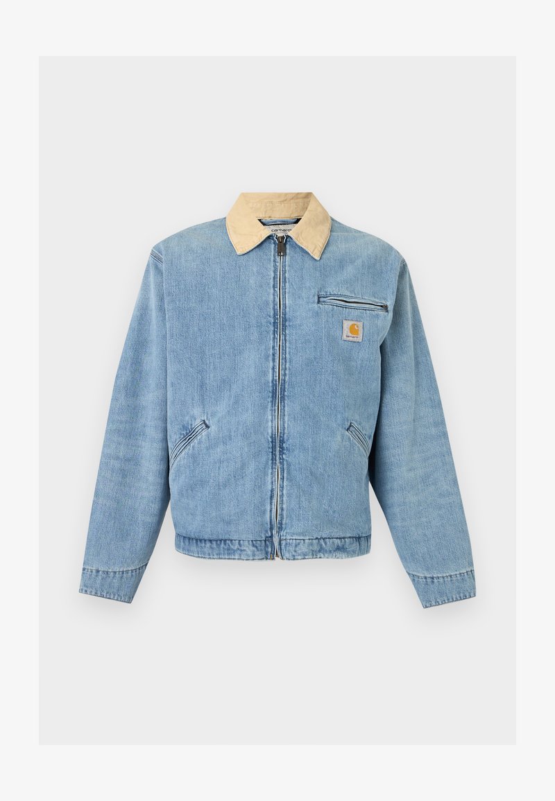 Lyseblå denimjakke med beige krave, lynlås foran, to nederste lommer, vandret lynlåslomme og Carhartt-logo på brystet.