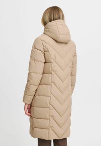 Piumino beige con cappuccio, caratterizzato da un motivo a rombi a imbottitura e maniche lunghe. Il cappotto arriva fino a metà polpaccio.