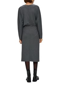 Robe grise avec une taille cintrée et de longues manches amples. Le tissu semble texturé. Portée avec des bottines noires à la cheville. Fermeture éclair dans le dos visible.