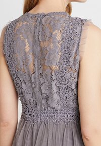 Robe en dentelle grise avec motifs floraux, tissu transparent, encolure arrondie et détails en mesh sur le dos et l'ourlet.